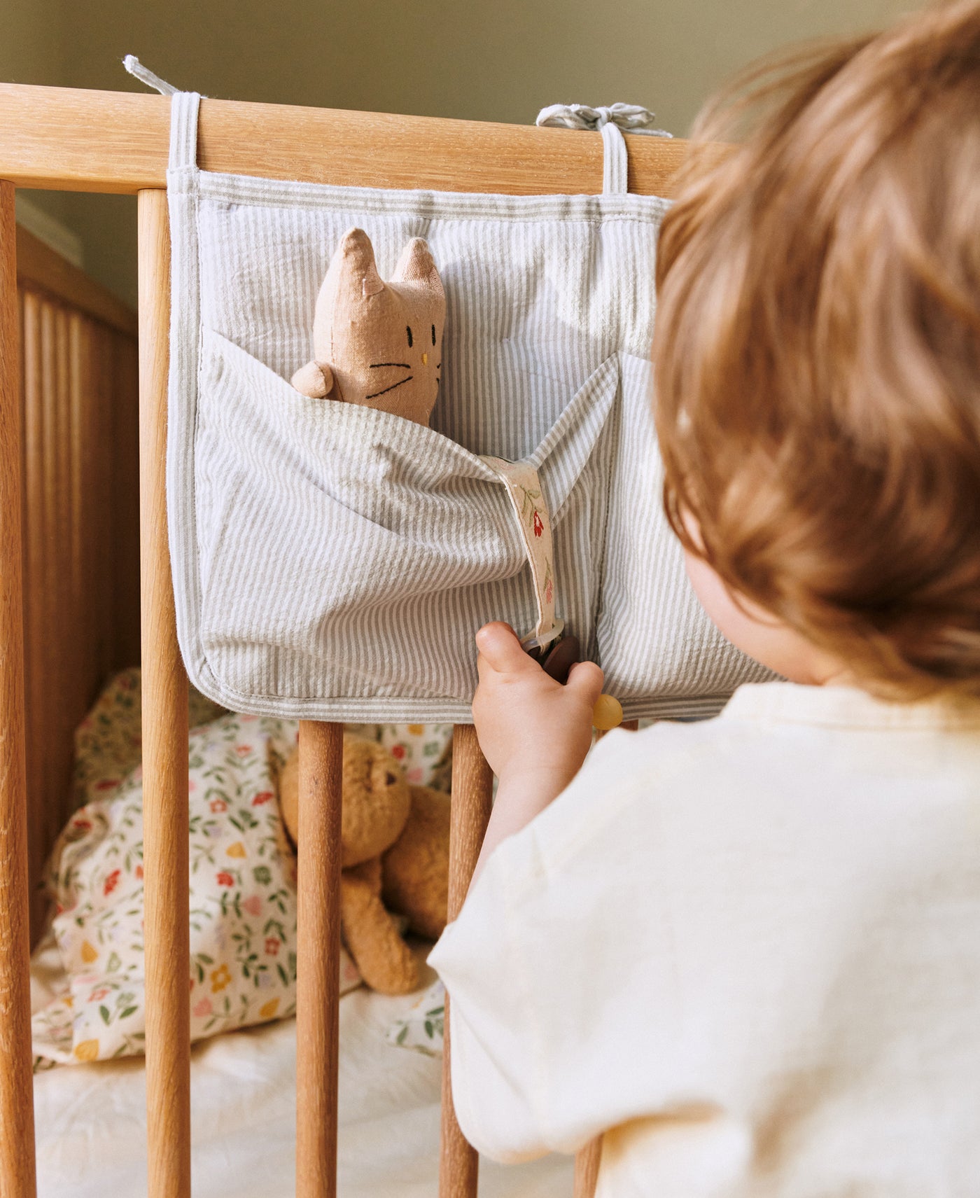 Toddler at the cot with a Dear April Dew Stripe bed pocket and cat toy